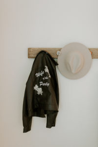 Black Leather Personalized Embroidered "Wife of the Party" Bride Jacket Hanging Next to Neutral Cowboy Hat Wedding Accessories
