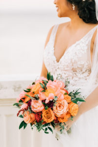 Tampa Bay Bride in Classic Lace Plunging V Neckline Tule A-Line Wedding Dress Holding Vibrant Colorful Orange and Pink Floral Bouquet
