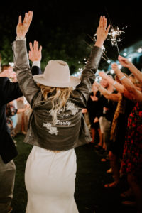 Fun Bride Wearing Black Leather Embroidered "Wife of the Party" Jacket Over Wedding Dress and Cowboy Monroe Rancher Hat