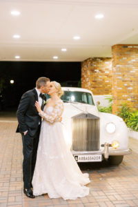 Classic Florida Bride and Groom Kiss In Front of Vintage 1960s Rolls Royce Getaway Car, Bride Wearing Adam Zohar A Line Wedding Dress with Illusion Lace Sleeves. Groom Wearing Black Giorgio Armani Bowtie Tuxedo | Tampa Bay Wedding Dress Boutique Isabel O'Neil Bridal Collection | Clearwater Country Club Wedding Planner Parties A'La Carte