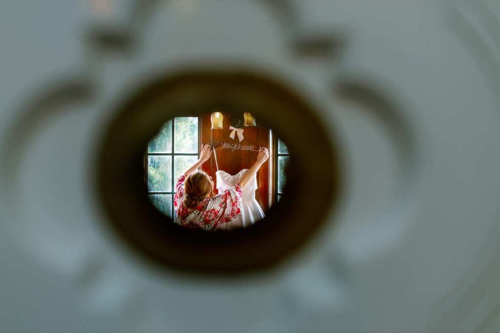 Unique Keyhole Photo Looking at Bride Hanging Up Wedding Dress | Tampa Bay Wedding Photographer Dewitt for Love Photography