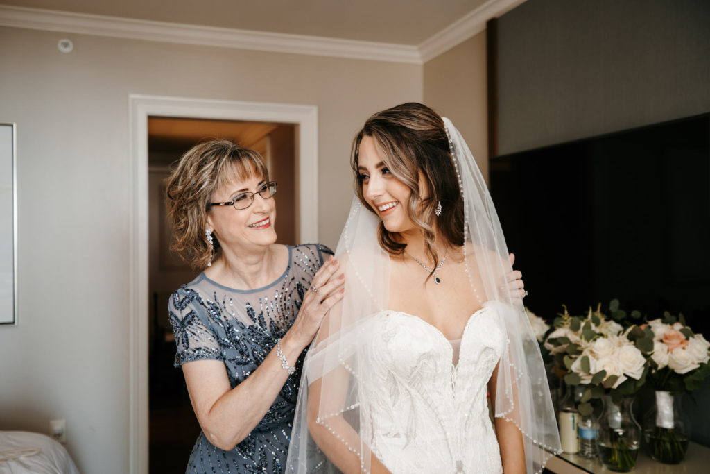 Bride Wearing Badgley Mischka Sweetheart Neckline Embroidered Floral Lace Wedding Dress and Beaded Trim Veil Getting Ready with Mom | Tampa Bay Wedding Dress Shop Truly Forever Bridal