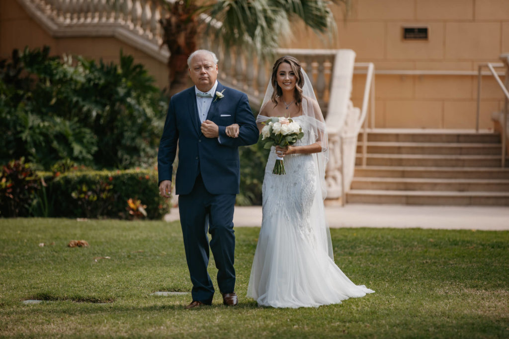 Bride Wearing Off the Shoulder Embroidered Floral Lace Badgley Mischka Wedding Dress Walking Down the Wedding Ceremony Aisle | Wedding Dress Shop Truly Forever Bridal