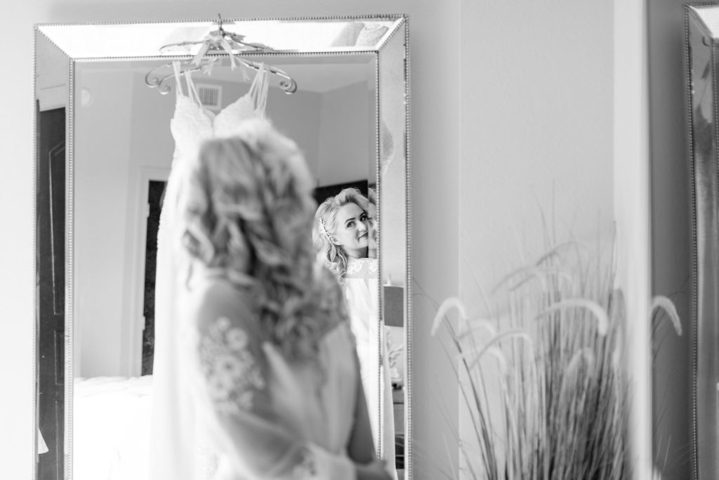 Bride Getting Wedding Ready Looking at Wedding Dress Hanging on Mirror | Tampa Bay Wedding Hair and Makeup Femme Akoi Beauty Studio