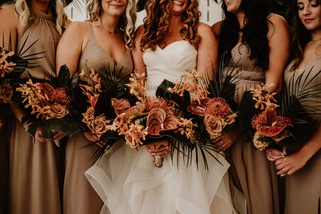 Elegant Bride and Bridesmaids Wearing Mix and Match Beige Dresses Holding Tropical Palm Fronds, Dusty Rose Roses, Orange Pin Cushion Flower, Anthurium, Palm Tree Leaves Circular Arch | Tampa Bay Wedding Florist Iza's Flowers