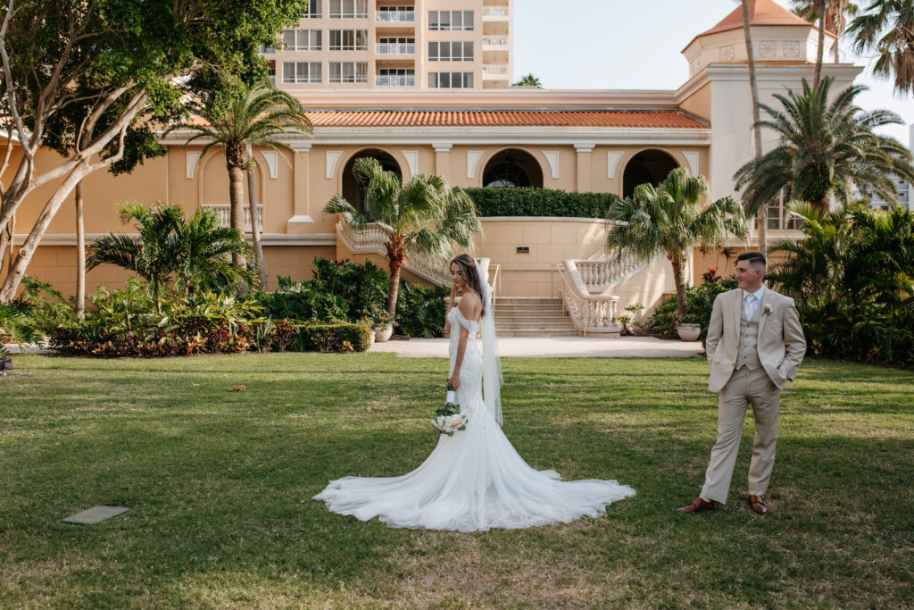 Bride Wearing Off the Shoulder Badgley Mischka Wedding Dress, Groom Wearing Tan Suit Outside Wedding Venue Ritz Carlton Sarasota | Tampa Bay Wedding Dress Shop Truly Forever Bridal