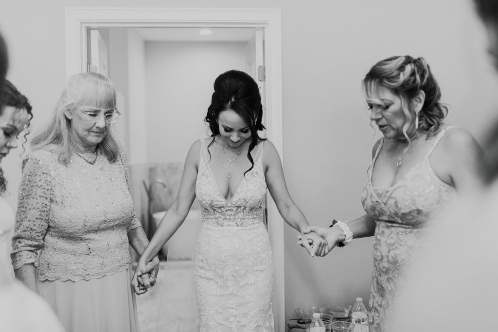 Bride Wearing Plunging V Neckline Lace and Illusion Wedding Dress in Prayer Circle with Family Before Wedding | Tampa Bay Wedding Photographer Amber McWhorter Photography