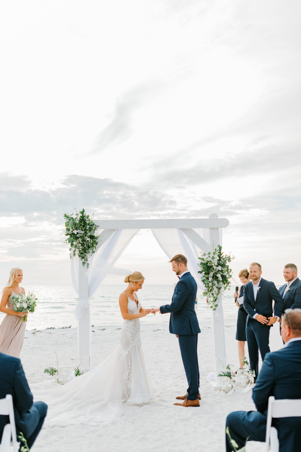 Florida Bride and Groom Exchanging Wedding Vows on Beach under White Arch with Greenery Arrangements and White Drapery | Tampa Wedding Venue The Resort at Longboat Key Club