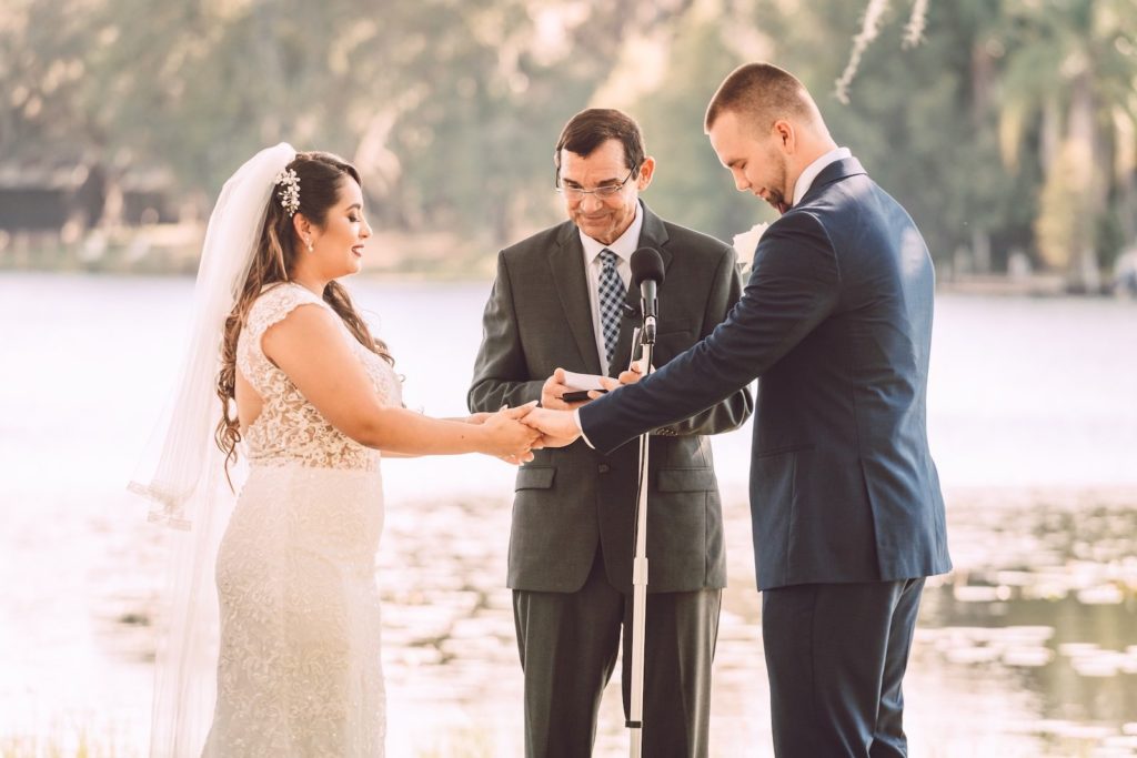 Florida Bride and Groom Exchanging Wedding Vows Lake Waterfront Ceremony | Tampa Bay Wedding Photographer Bonnie Newman Creative | Wedding Dress Shop Truly Forever Bridal | Odessa Wedding Venue Barn at Crescent Lake