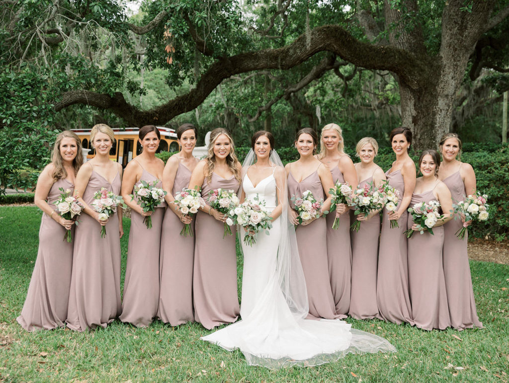 Classic Bride Wearing Paloma Blanca Spaghetti Strap Fit and Flare V Neckline Wedding Dress, Full Length Veil, Bridesmaids in Matching Mauve Dresses Holding White Roses and Eucalyptus Floral Bouquets | Tampa Bay Wedding Hair and Makeup Femme Akoi Beauty Studio | Bridesmaids Dresses Bella Bridesmaids