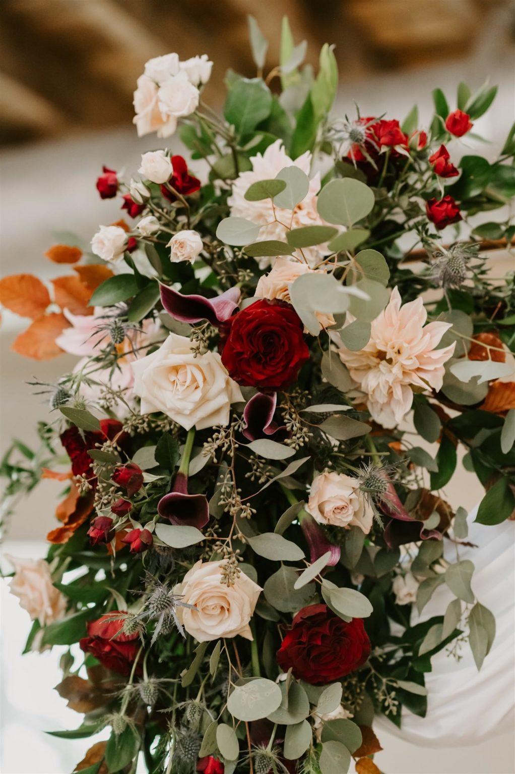Draped Wedding Ceremony Arch with Fall Greenery Floral Arrangement Spray of Copper Leaves, White and Red Roses, Zinnia, and Eucalyptus | Botanica International Design
