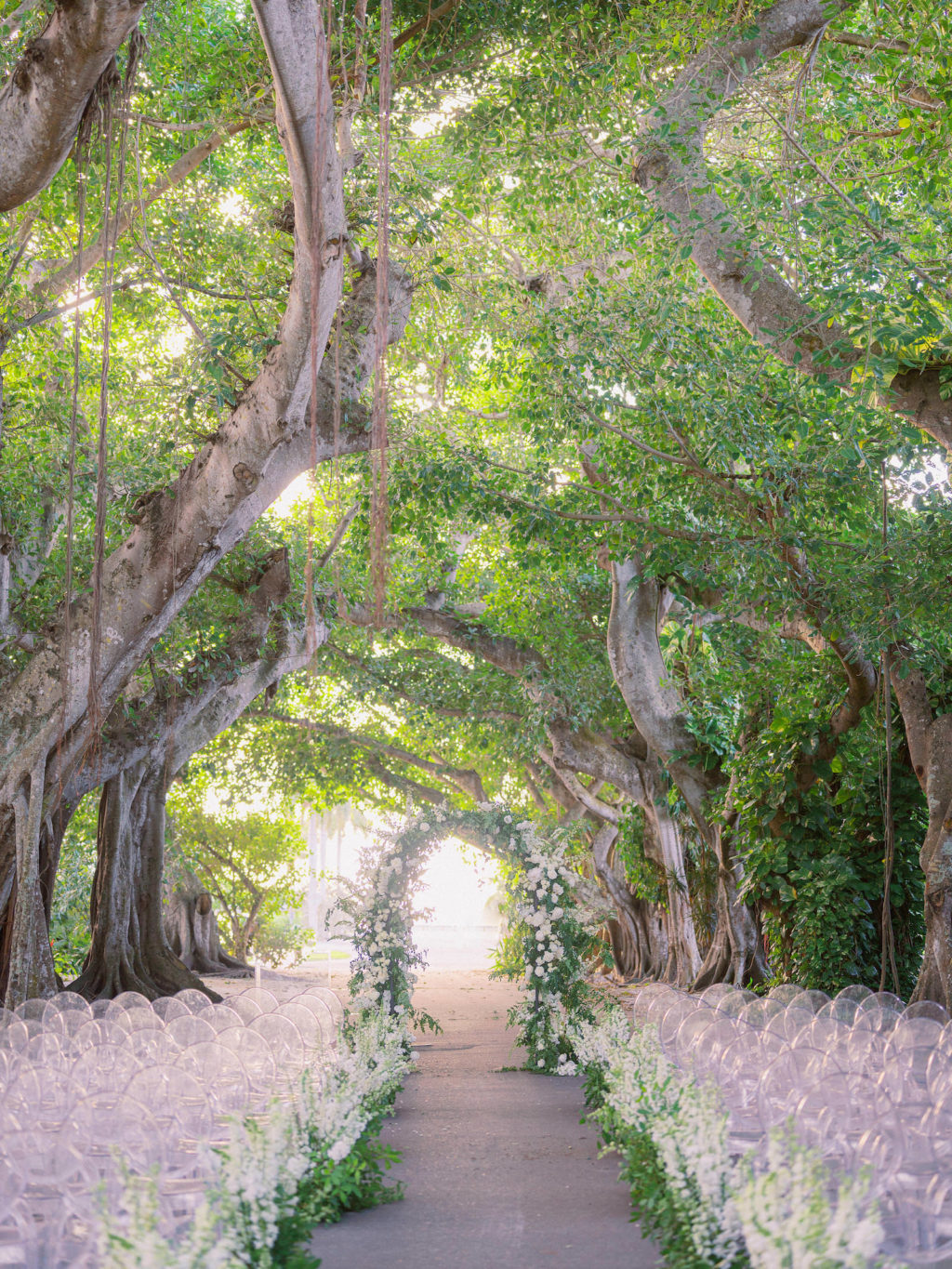 Elegant Luxurious Classic Outdoor Wedding Ceremony Decor Under Banyan Trees, Acrylic Ghost Chairs with Lush White and Greenery Floral Arrangements, Semi Circle Flower and Greenery Wedding Ceremony Arch | Tampa Bay Wedding Venue The Gasparilla Inn and Club