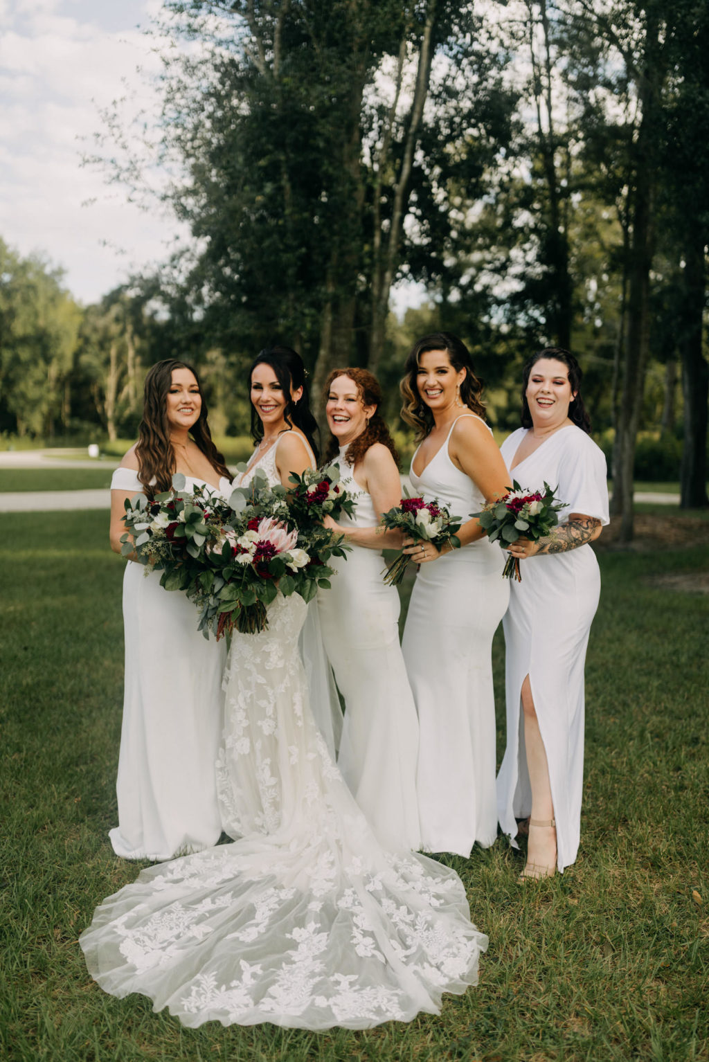 Bride and Bridesmaids Wearing Mix and Match White Dresses Holding Dark and Moody Garden Inspired Greenery with Pink King Proteas Floral Bouquets | Tampa Bay Wedding Photographer Amber McWhorter Photography | Outdoor Wedding Venue Paradise Spring | Wedding Florist Brides & Blooms