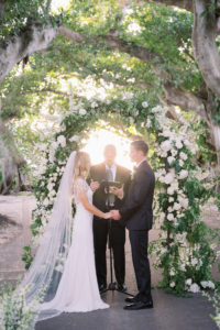 Classic Florida Bride and Groom Exchanging Wedding Vows Lush White Floral and Greenery Leaves Semi Circle Arch | Boca Grande Wedding Venue The Gasparilla Inn and Club