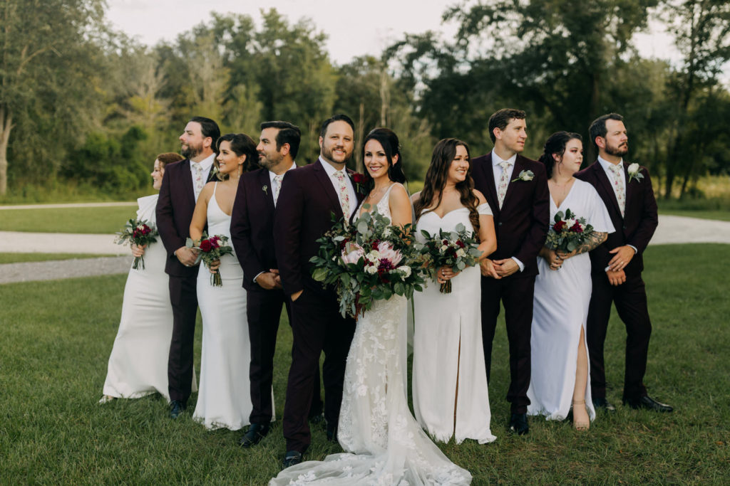 Dark and Moody Bride Holding Garden Inspired Floral Bouquet with Greenery, Pink King Proteas, Red and Ivory Flowers, Groom in Dark Red Suit and Floral Pattern Tie, Bridesmaids in Mix and Match White Dresses, Groomsmen in Maroon Suits | Tampa Bay Wedding Photographer Amber McWhorter Photography | Wedding Florist Brides & Blooms