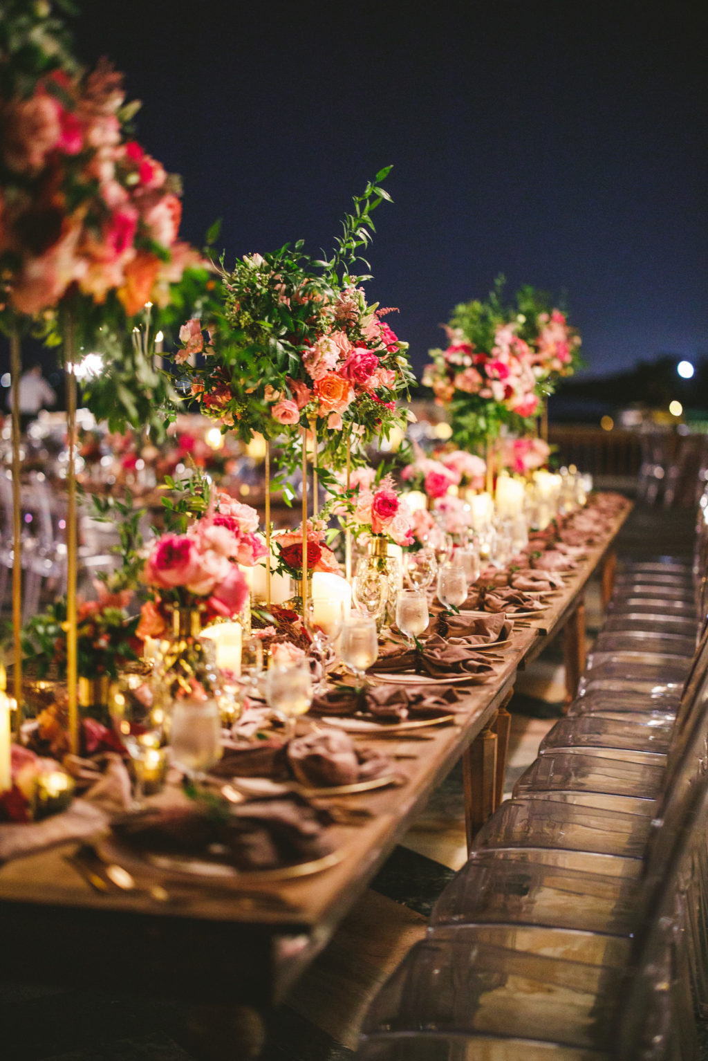 Luxury Elegant Tampa Wedding Reception with Long Feasting Tables featuring Colorful Blush Pink, Fuchsia and Orange Rose Centerpieces with Greenery and Candles and Clear Ghost Chairs