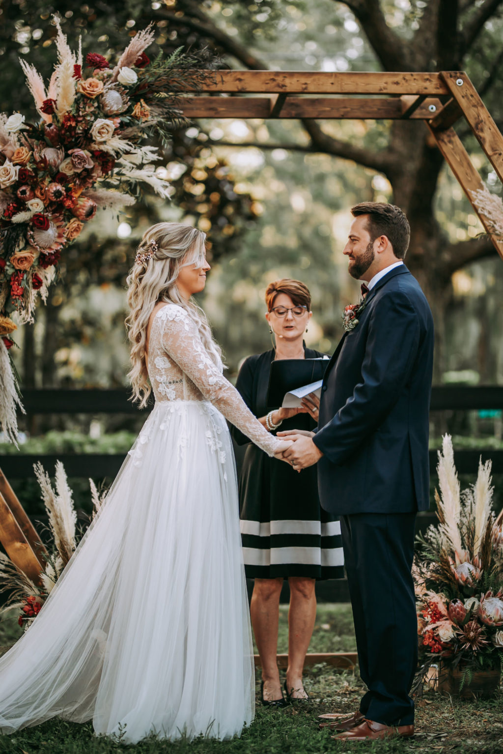 Rustic Florida Bride and Groom Exchanging Wedding Vows Under Wooden Hexagonal Ceremony Arch with Lush Floral Arrangements