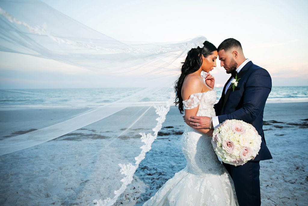 Florida Bride and Groom Veil Blowing in Wind at Beach Wedding Portraits at Sunset, Bride wearing Rivni Fit and Flare Wedding Dress, Holding Traditional Round Wedding Bouquet, | The Don CeSar in St. Pete Beach | Tampa Bay Wedding Photography Limelight Photography | Florida Wedding Florist Iza's Flowers | South Tampa Bridal Boutique Isabel O'Neil Bridal