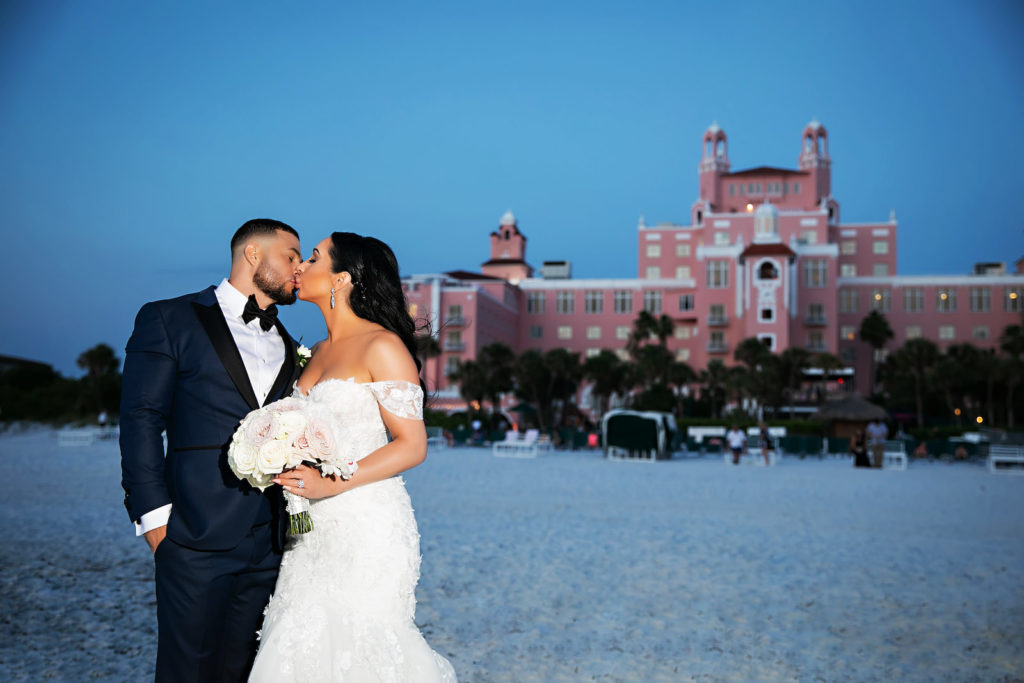Florida Bride and Groom Kissing on Beach at Sunset, Bride Holding Round Bouquet and Wearing Rivini Wedding Dress | The Don CeSar in St. Pete Beach | Tampa Bay Wedding Photography Limelight Photography | Florida Wedding Florist Iza's Flowers