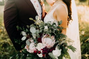 Sunset Groom and Bride Holding Lush Wild Garden Floral Bouquet with Greenery, Eucalyptus, Blush Pink King Proteas, White Roses and Dark Red Flowers | Tampa Bay Wedding Photographer Amber McWhorter Photography | Wedding Florist Brides & Blooms