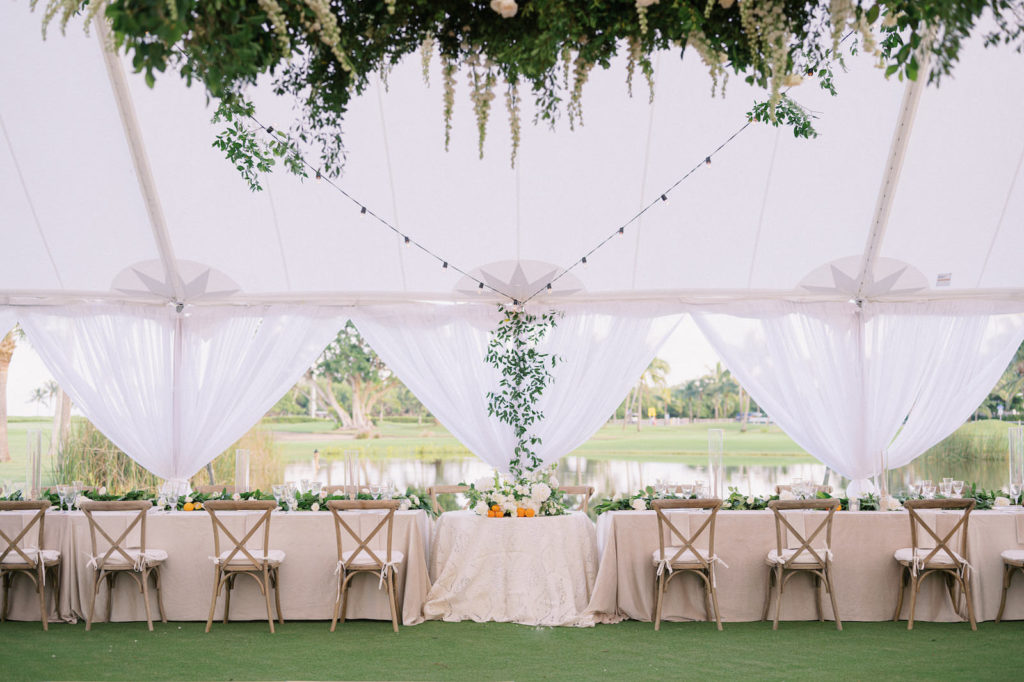 Elegant Florida Classic Luxurious Outdoor Tent Wedding Reception Decor, Long Feasting Table with Taupe Linens, Wooden Cross Back Chairs, White Linen Drapery, String Lights, Lush Greenery Chandelier Arrangement | Boca Grande Wedding Venue The Gasparilla Inn and Club