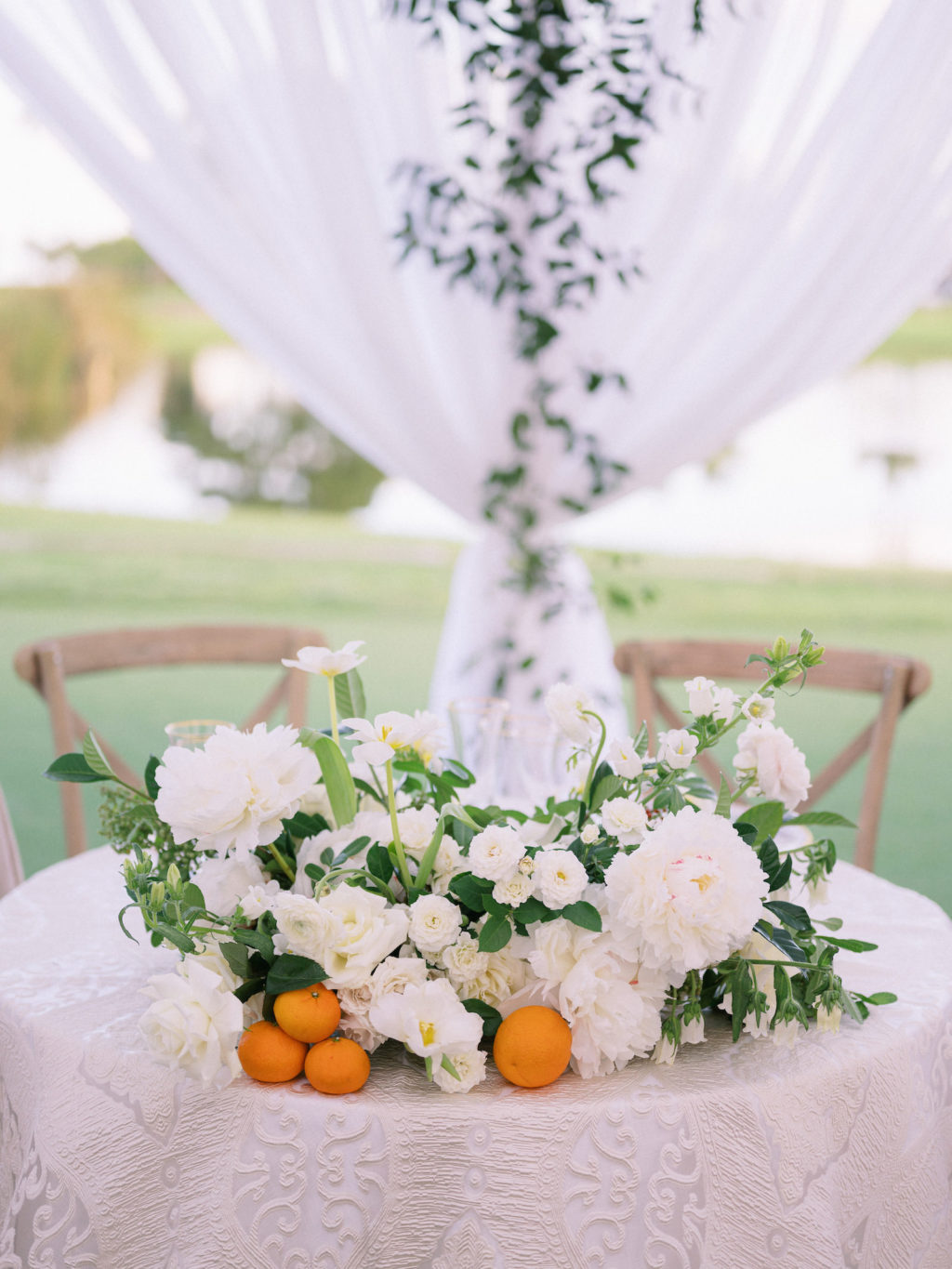 Elegant Luxurious Classic Florida Wedding Reception Decor, Table with Decorative Table Linen, Lush White Flower and Greenery Leaves Bouquet with Oranges, Wooden Cross Back Chairs