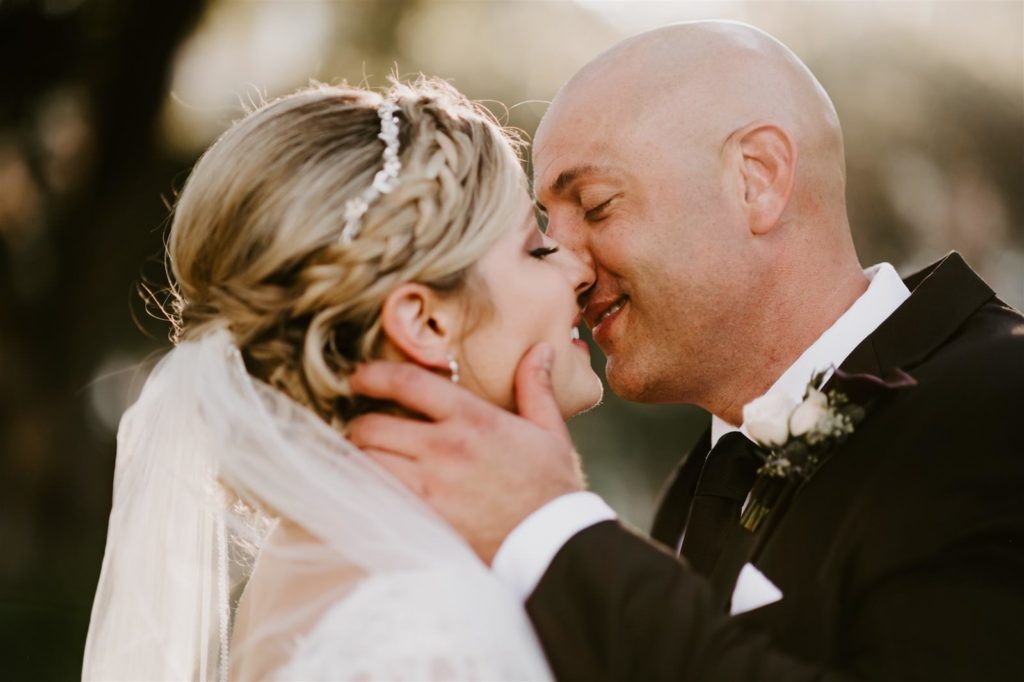 Outdoor Bride and Groom Sunset Portrait Kiss | Bridal Hairstyle Updo with Crown Braid and Rhinestone Headband and Long Cathedral Veil