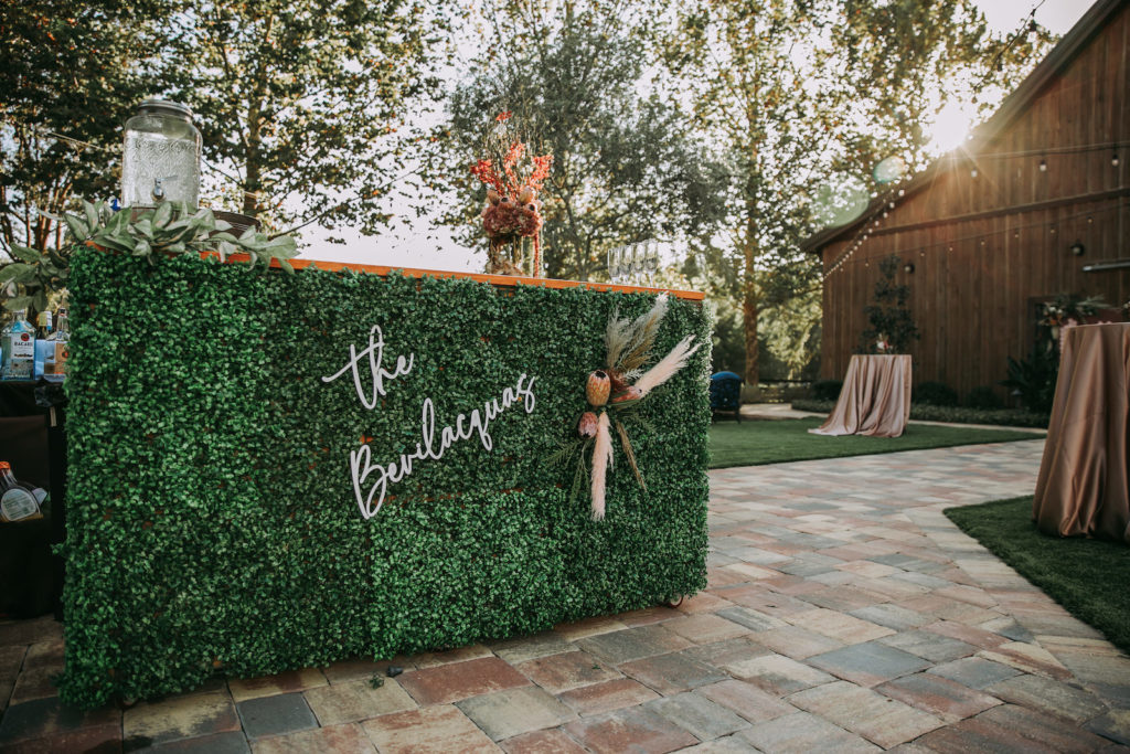 Rustic Barn Wedding Cocktail Decor, Greenery Hedge Wall Bar with Custom Laser Cut Last Name, Floral Arrangement of Pampas Grass and King Proteas | Tampa Bay Wedding Venue Mision Lago Estate | Mision Lago Ranch