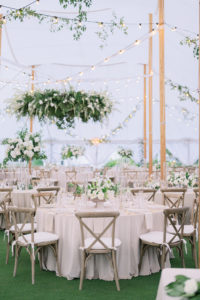 Luxurious Elegant Florida Classic Outdoor Tent Wedding Reception Decor, White Linen Draping, String Lights and Hanging Greenery, Wooden Cross Back Chairs, Tall White Flower and Greenery Tall Floral Centerpieces