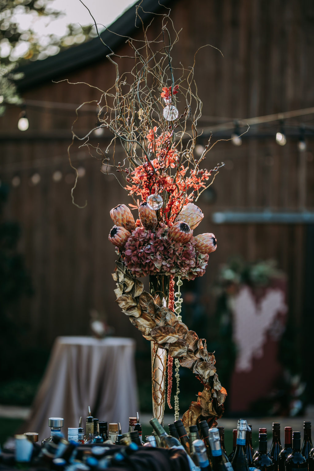 Rustic Unique Wedding Floral Arrangement, Closed King Proteas, Wooden Whimsical Sticks, Glass Bulbs Hanging, Curved Leaves and Hanging Amaranthus
