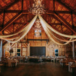 Rustic Florida Barn Wedding Reception, Draped Linens on Ceiling with String Lights, Deer Antler Chandeliers, Long Feasting Table for Wedding Party and Round Tables for Guests | Tampa Wedding Venue Mision Lago Estate | Mision Lago Ranch