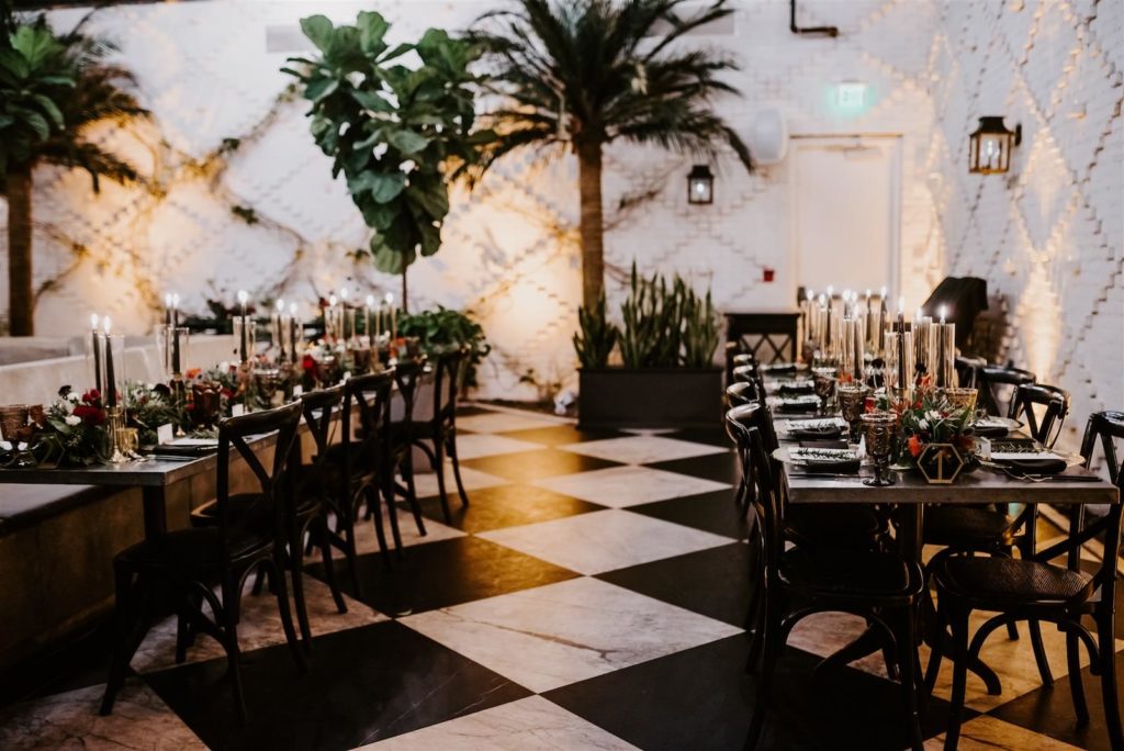 Downtown Tampa Industrial Intimate Historic Wedding with Atrium Conservatory Dinner Reception under Canopy of String Lights | Long Feasting Banquet Tables with Black and Gold Candlesticks and Black Cross Back Chairs | Botanica International Design | Winsor Event Studio