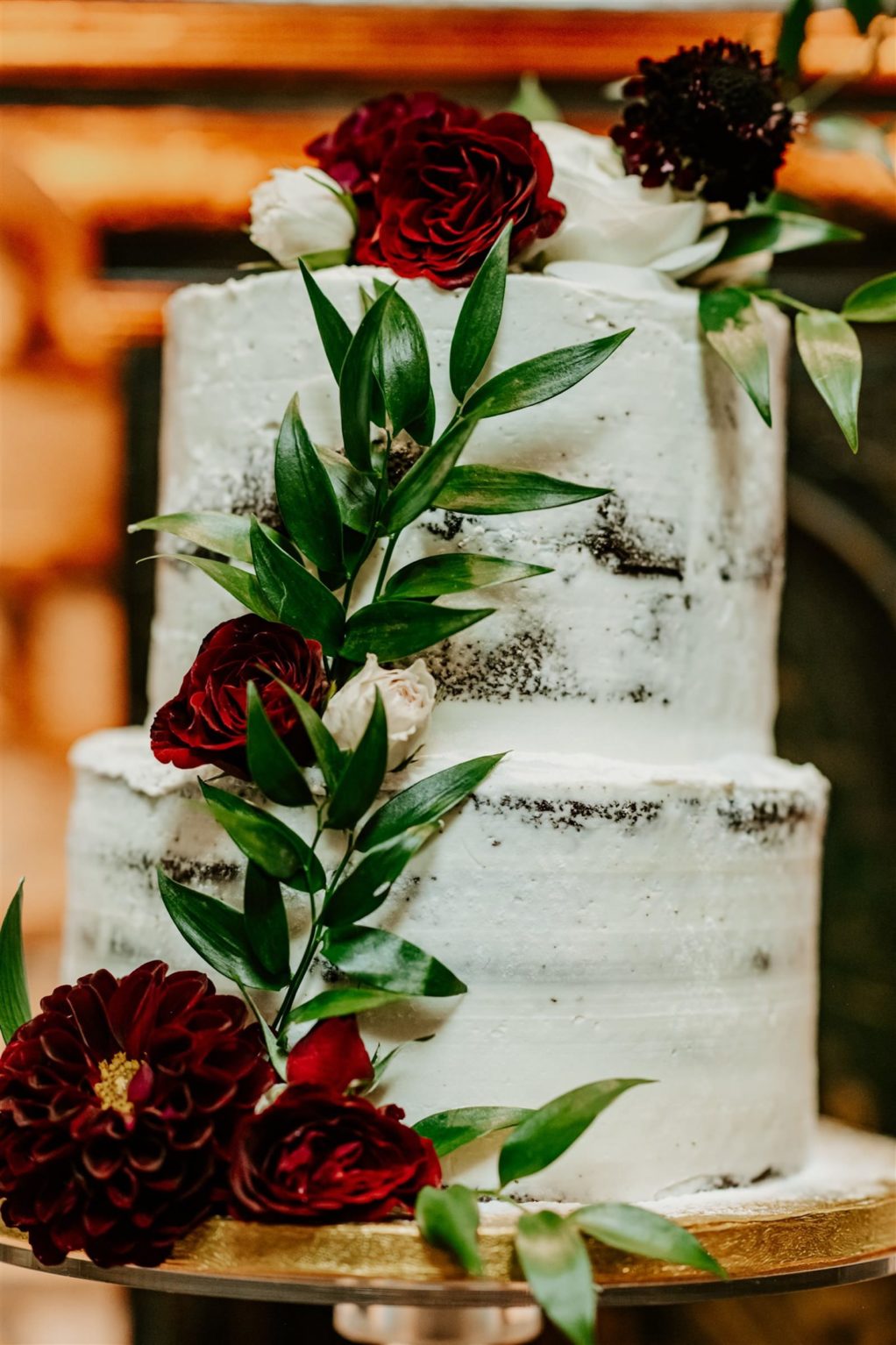 Two Tier Semi Naked Buttercream Wedding Cake with Greenery and Deep Red Ranunculus and Roses
