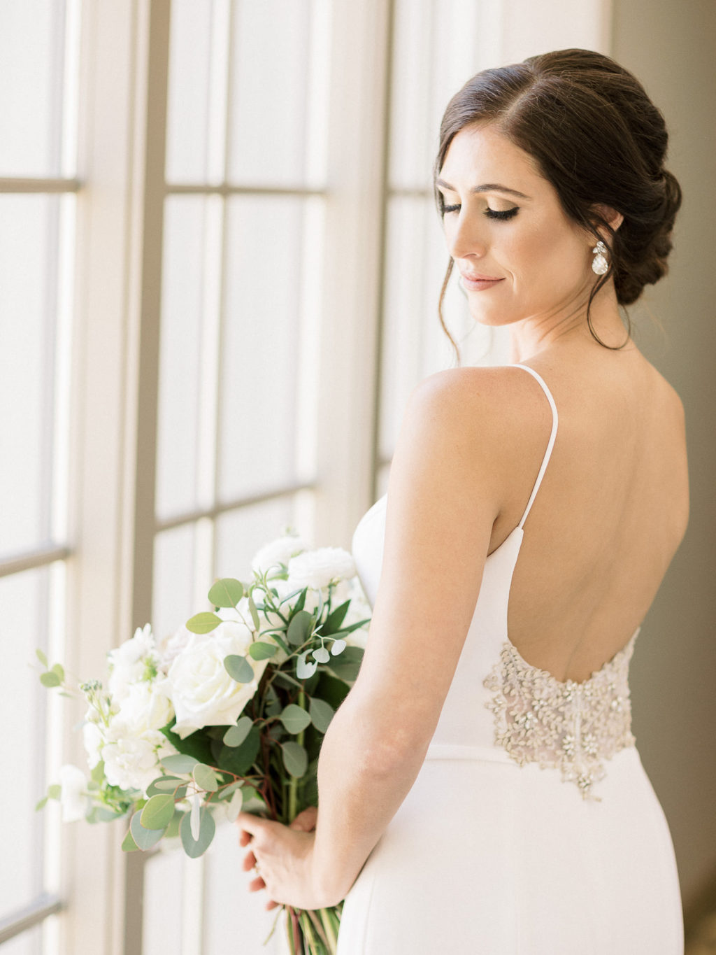 Florida Bride Wearing Classic Spaghetti Strap Open Back with Beige Floral and Illusion Lace/Rhinestone Paloma Blanca Wedding Dress Holding White Roses and Eucalyptus Floral Bouquet | Tampa Bay Wedding Hair and Makeup Femme Akoi Beauty Studio
