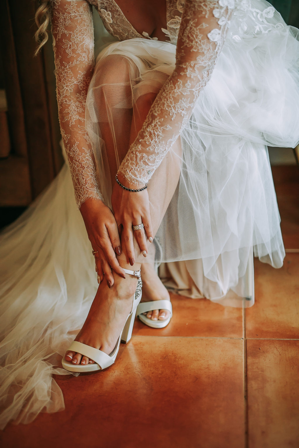 Florida Bride Getting Wedding Ready Putting on Ivory Block Heel Wedding Shoes Wearing Lace and Illusion Long Sleeve Wedding Dress