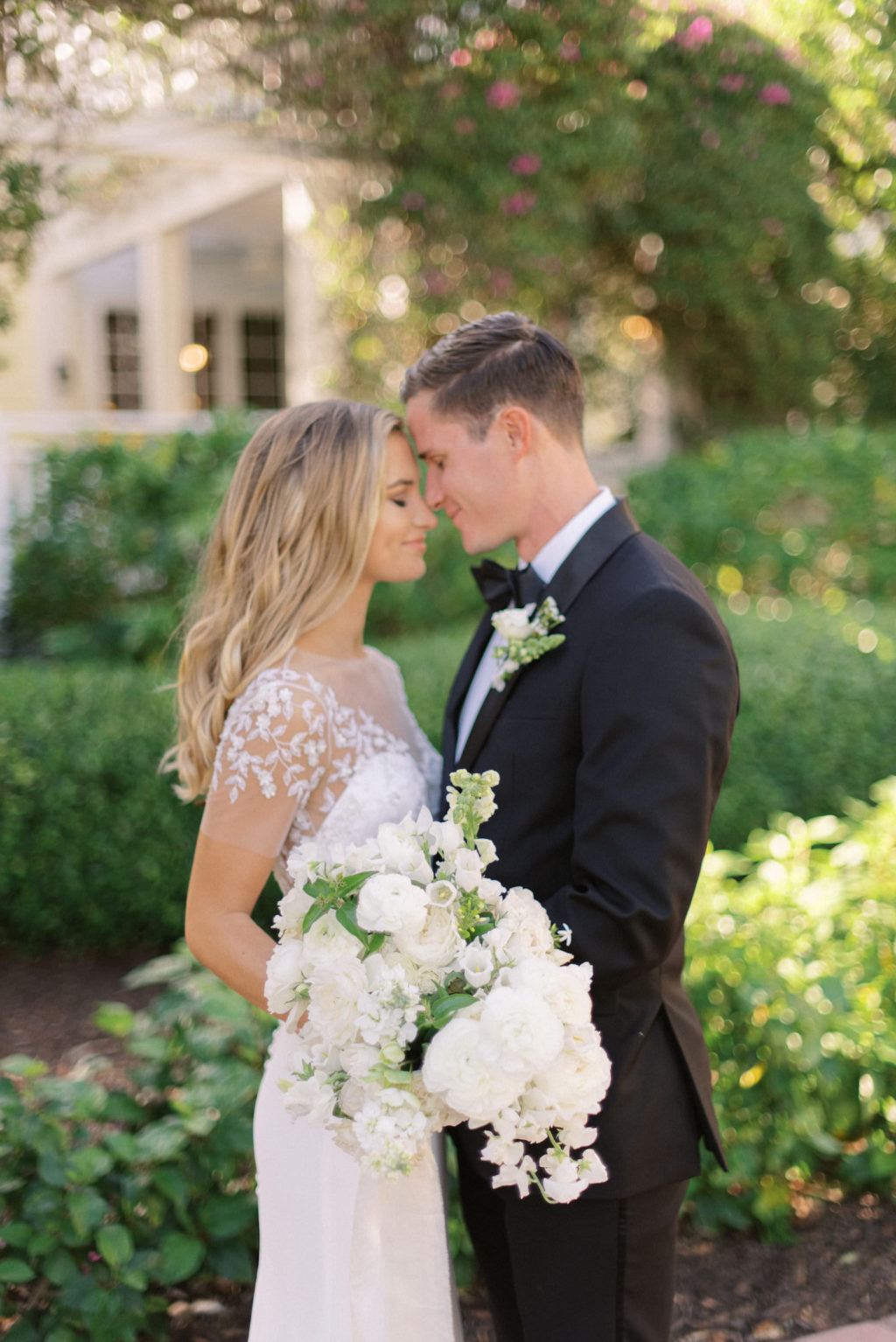Florida Groom in Black Tuxedo and Bride Wearing Suzanne Neville Mayflower Illusion and Delicate Floral Lace Embellishment Cap Sleeve and Crepe Fitted Wedding Dress Holding Classic Lush White Floral Bouquet