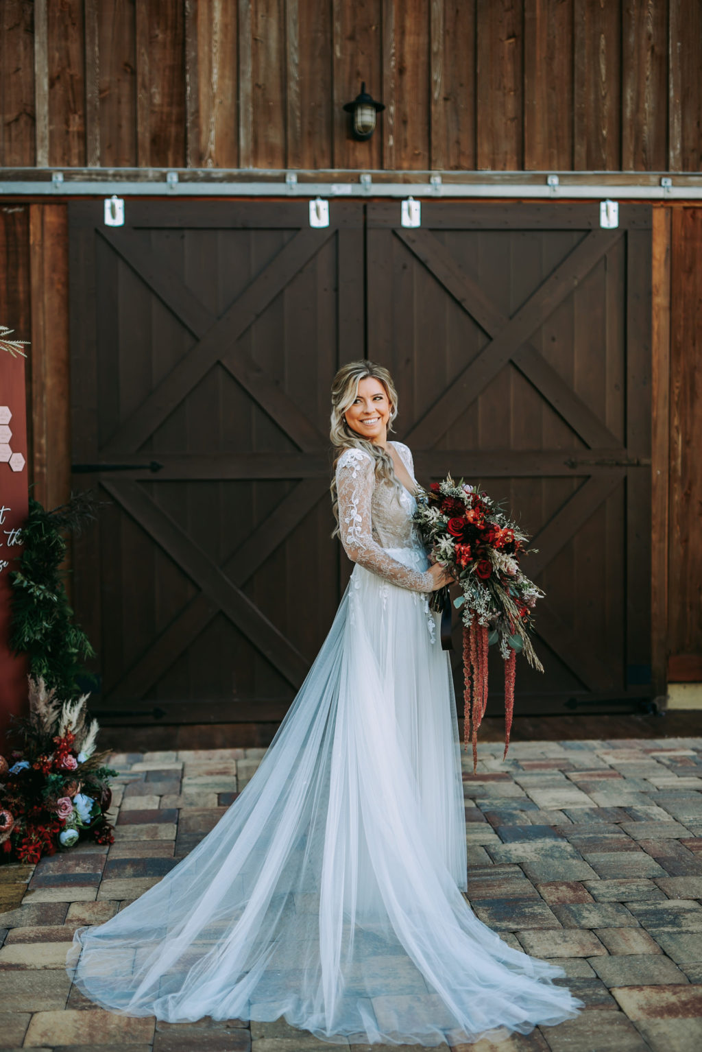 Rustic Bride Wearing Lace and Illusion Long Sleeve Wedding Dress Holding Burgundy Red Flowers, Greenery and Hanging Amaranthus Bouquet | Tampa Wedding Venue Mision Lago Estate