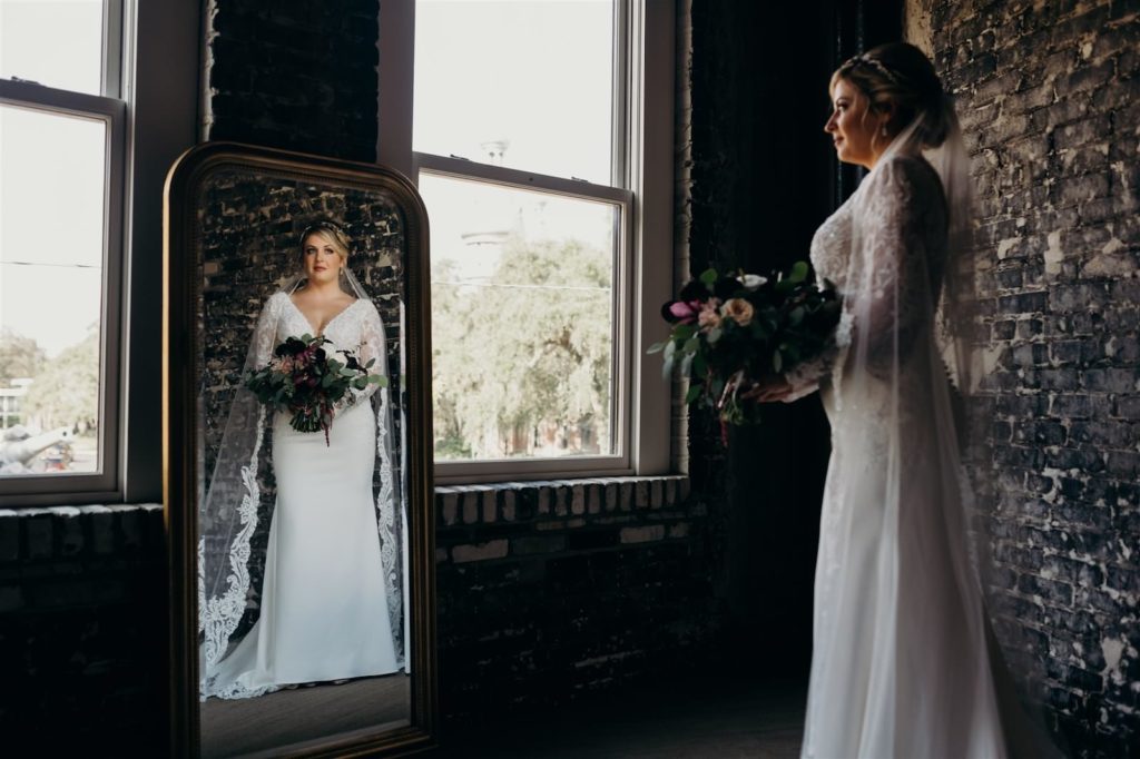 Indoor Bridal Portrait in Mirror | Rhinestone Bridal Headband Updo Chignon Hairstyle | V Neck Long Sleeve Lace Sheath Bridal Gown with Long Cathedral Lace Veil