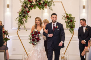 Florida Bride and Groom Exiting Wedding Ceremony First Kiss Under Gold Geometric Hexagonal Arch with Greenery and Blush Pink, Burgundy Roses | Tampa Bay Wedding Planner Coastal Coordinating