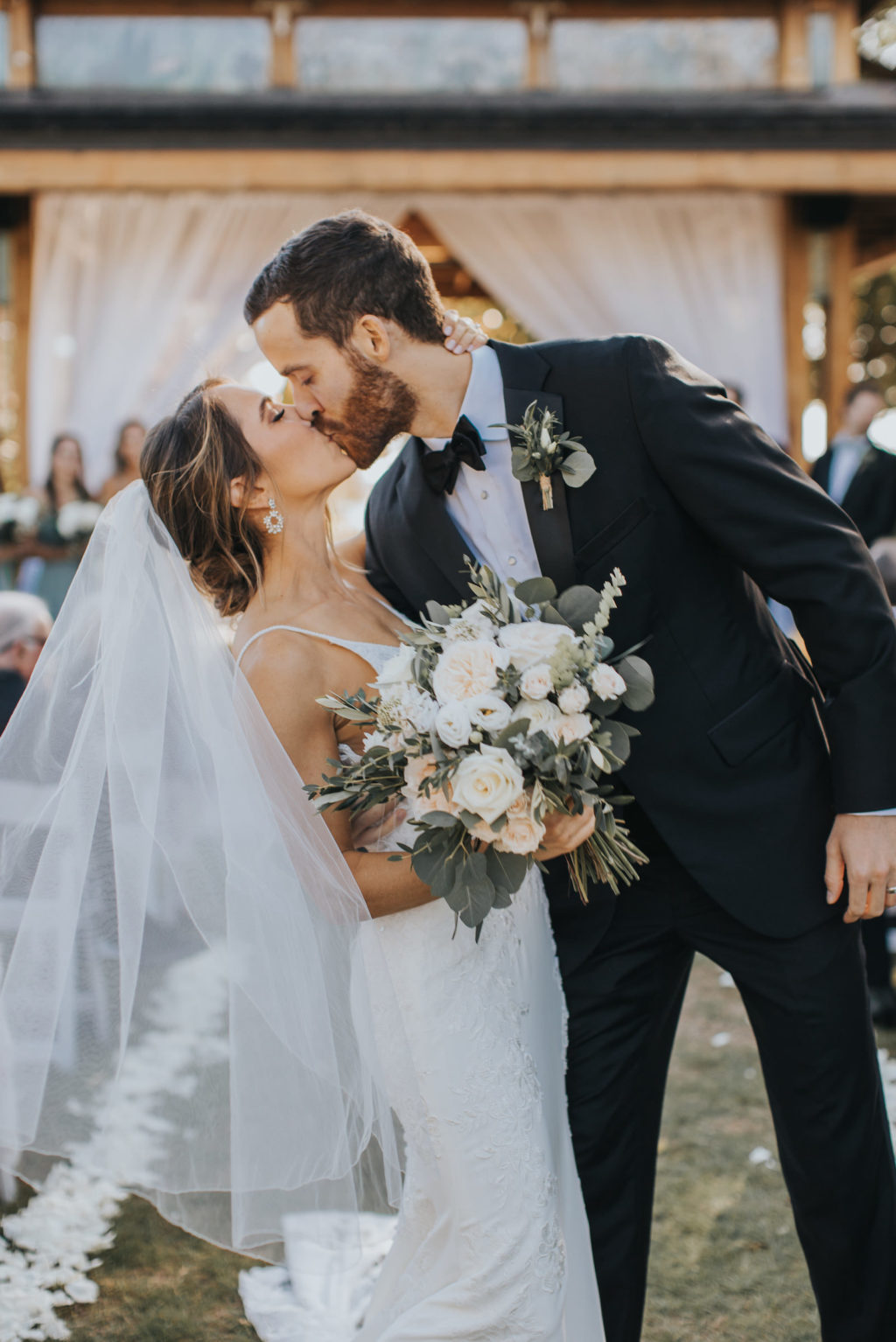 Bride and Groom First Kiss Ceremony Portrait | Bride in Essense of Australia Wedding Gown with Long Train Veil | White and Cream Florals with Greenery Bouquet