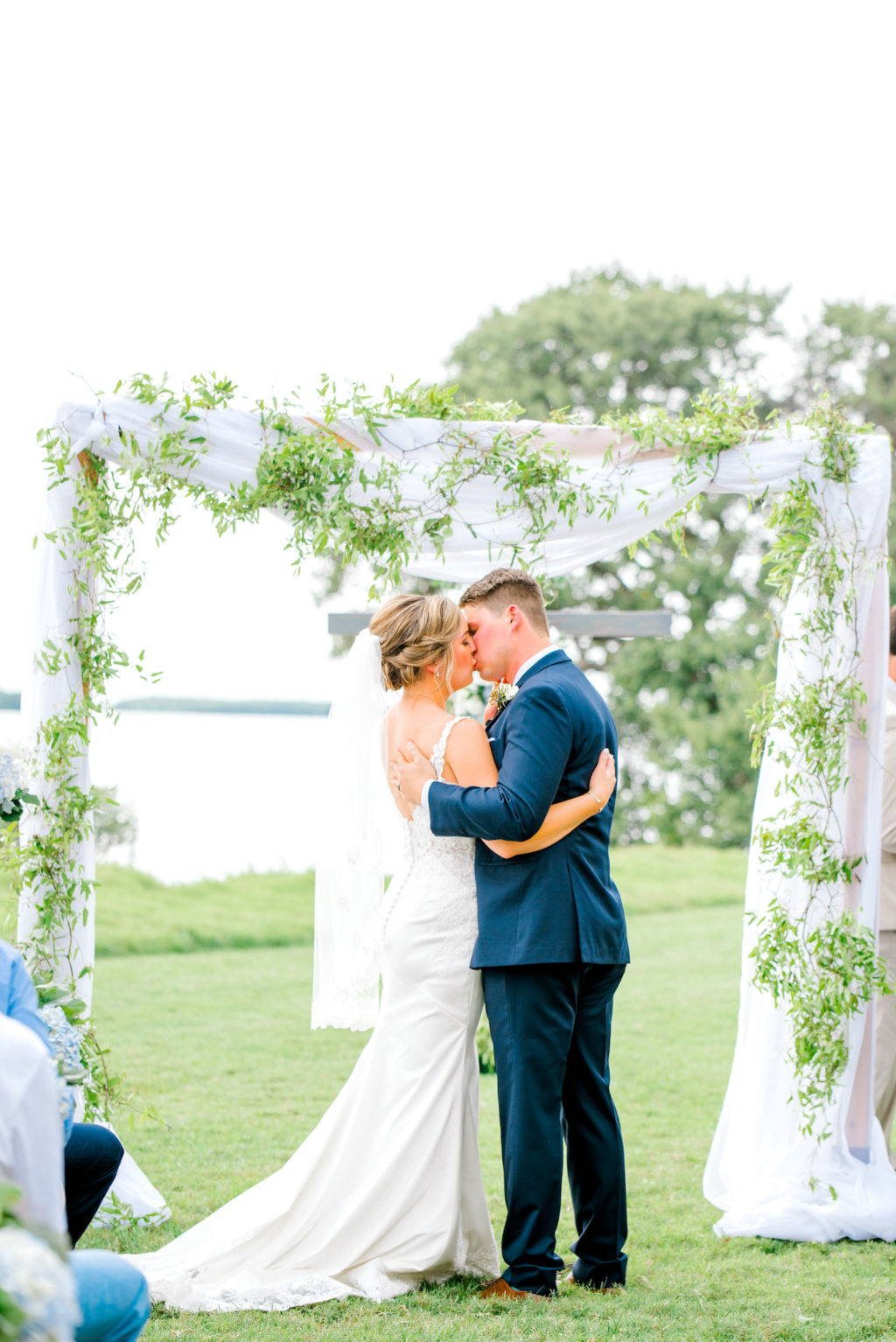 Bride and Groom First Kiss Under Beautiful Ceremony Arch with Greenery and Linen Draping | Tampa Bay Waterfront Wedding Ceremony