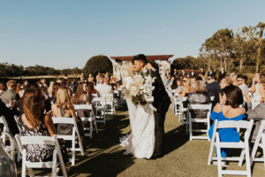 Timeless Bride and Groom Exiting Wedding Ceremony with Kiss in Aisle, Bride Holding Neutral Lush Floral Arrangement, King Proteas, Ivory Roses, Palm Fronds and Monstera Palm Leaves | Bradenton Wedding Venue The Concessions Golf Course