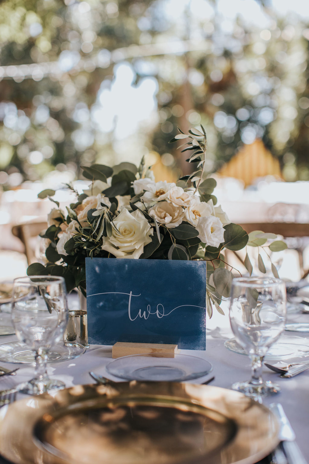 Blue Calligraphy Table Number with Gold Chargers and Ivory and Low Centerpieces with Greenery | Romantic Garden Wedding Reception Tablescape Inspiration