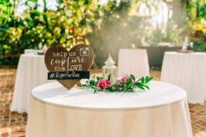 Rustic Wedding Cocktail Hour Décor | Hashtag Sign on White Linen and Circular Entrance Table | Vibrant Pink Centerpieces with Greenery