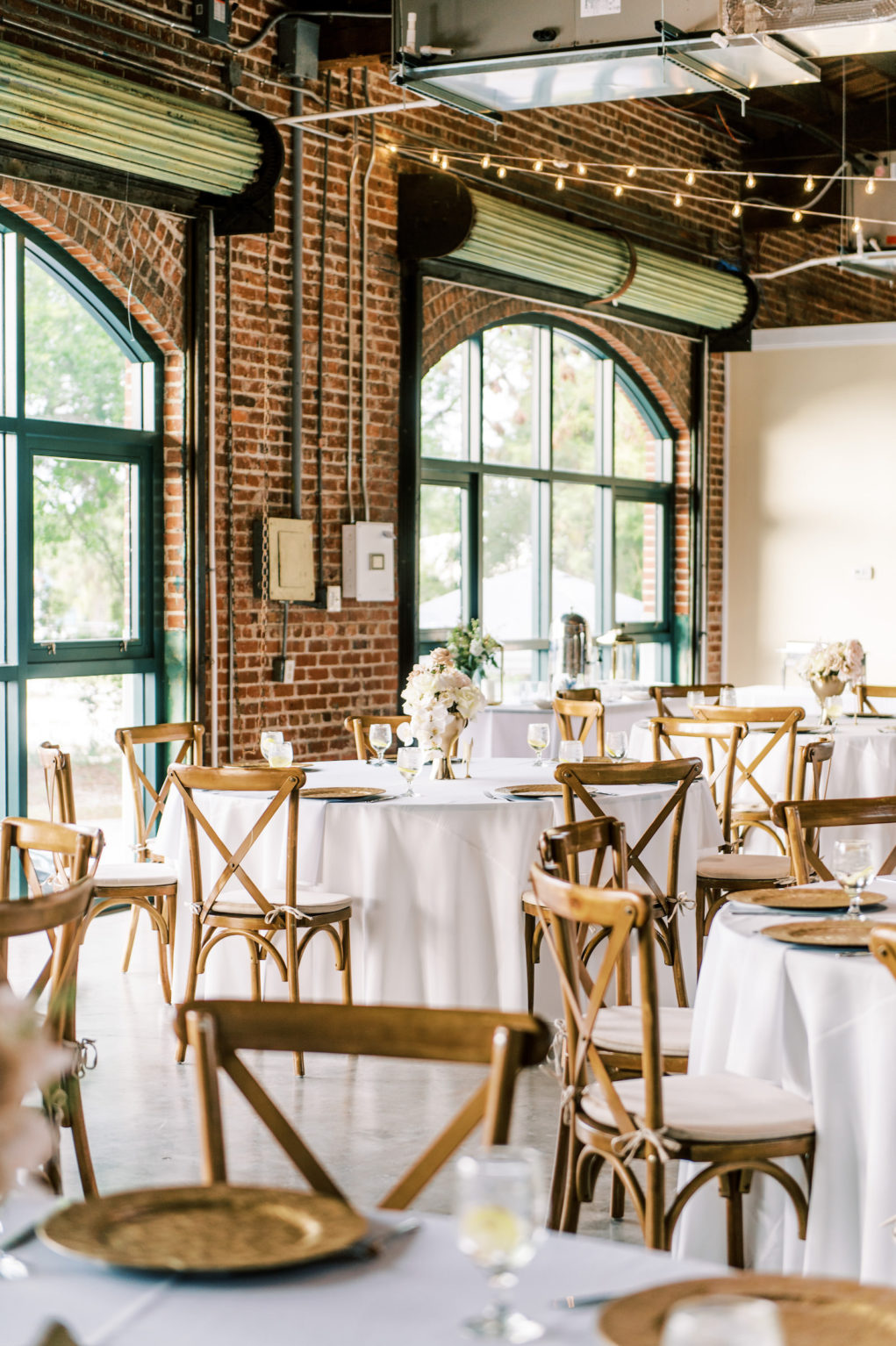 Classic Wedding Reception Decor, Round Tables with White Linens, Wooden Cross Back Chairs, Low Floral Centerpieces, String Lights | Tampa Bay Wedding Photographer Kera Photography | Wedding Caterer Olympia Catering | Wedding Rentals Gabro Event Services | St. Pete Wedding Venue Morean Center for Clay