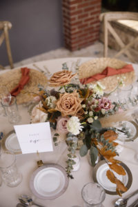 Wicker Place Mats with Burnt Orange Napkins on Cream Linen | Low Centerpieces with Roses, Greenery, and Pampas Leaves in Gold Holder | Bohemian Wedding Reception Decor for Tablescapes | Sarasota Rentals Kate Ryan Event Rentals