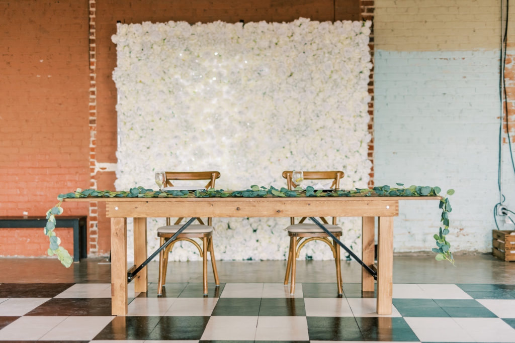 Simple Wedding Reception Decor, Wooden Long Table with Greenery Garland, Wooden Cross Back Chairs, White Floral Backdrop, Black and White Checkered Dance Floor | Tampa Bay Wedding Photographer Kera Photography | Wedding Rentals Gabro Event Services