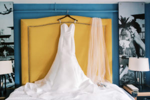 Classic Crepe Strapless Wedding Dress Hanging on Yellow Bed Headboard | Tampa Bay Wedding Photographer Kera Photography