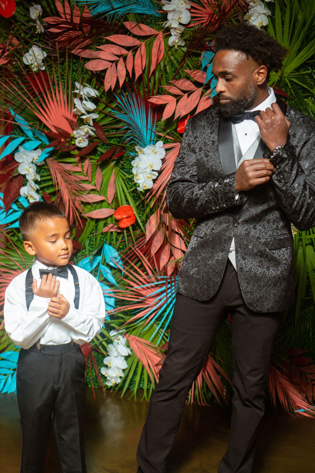 Dearly Beloved Fashion Show, Man and Boy Matching Suit and Bowtie, Groom Wearing Textured Jacket Designed by Royal Bridal, Modern Tropical Floral Wall with Green, Pink and Aqua Blue | Florida Wedding Venue 7th and Grove