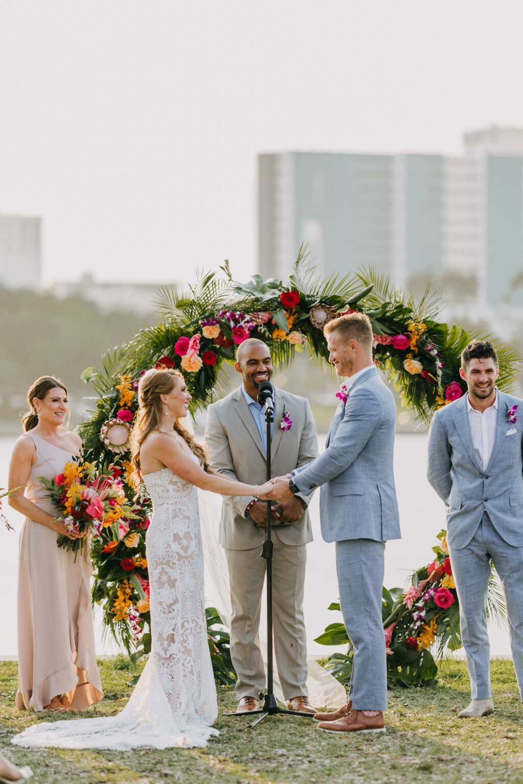 Bride and Groom Exchanging Wedding Vows During Waterfront Tropical Wedding Ceremony Decor, Circular Colorful Floral Arch | Tampa Bay Wedding Photographer Amber McWhorter Photography